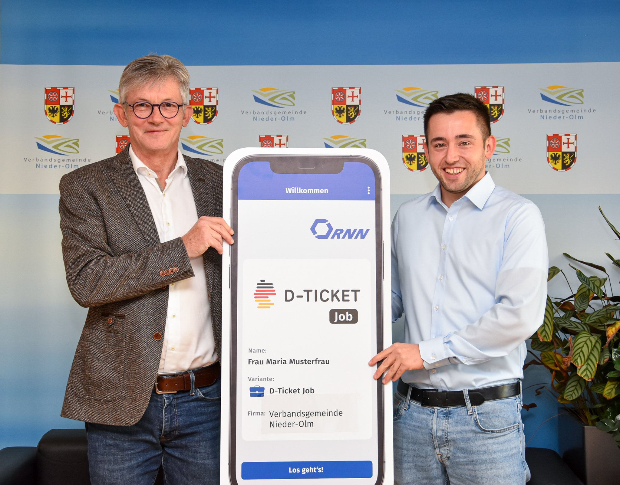 Auf dem Bild erkennt man zwei Männer. Links den Bürgermeister Ralph Spiegler und recht einen Angestellten des RNN. Beide halten in ihren Händen ein überdimensional großes Handy, auf welchem das Deutschland-Ticket Job zu sehen ist.