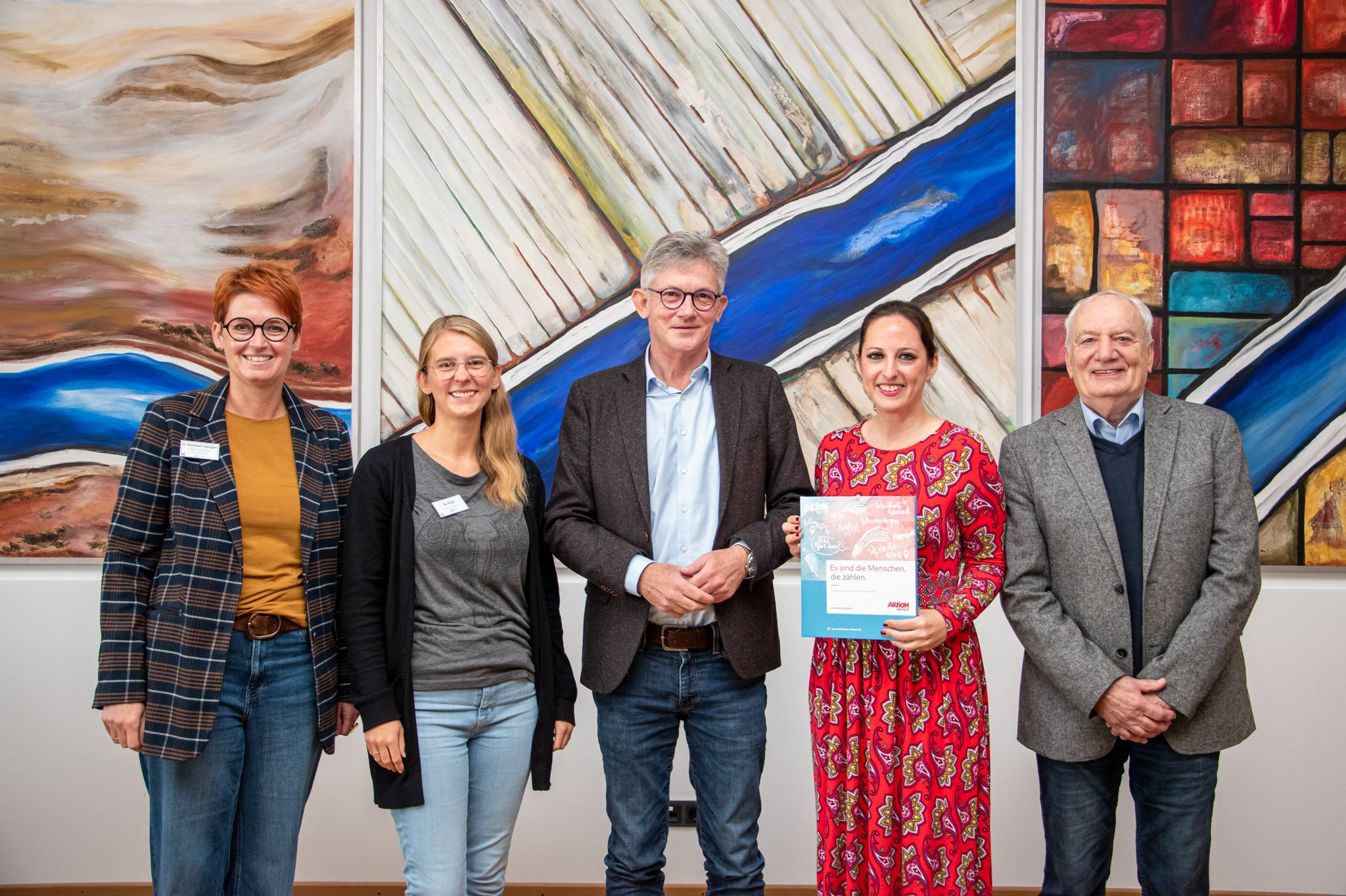 Auf dem Bild erkennt man fünf Personen, die frontal freudig in Richtung Kamera blicken.