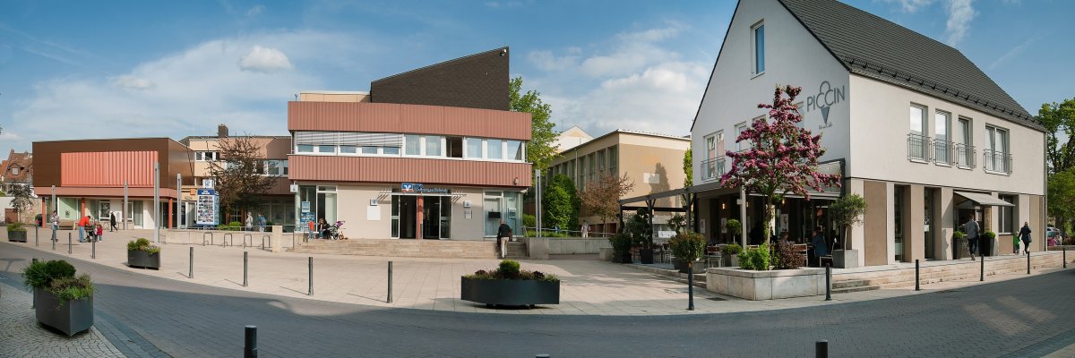 Auf dem Foto erkennt man den Rathausplatz von Nieder-Olm. Links das Rathaus, in der Mitte eine Volksbankfiliale und rechts ein Eiscafé.