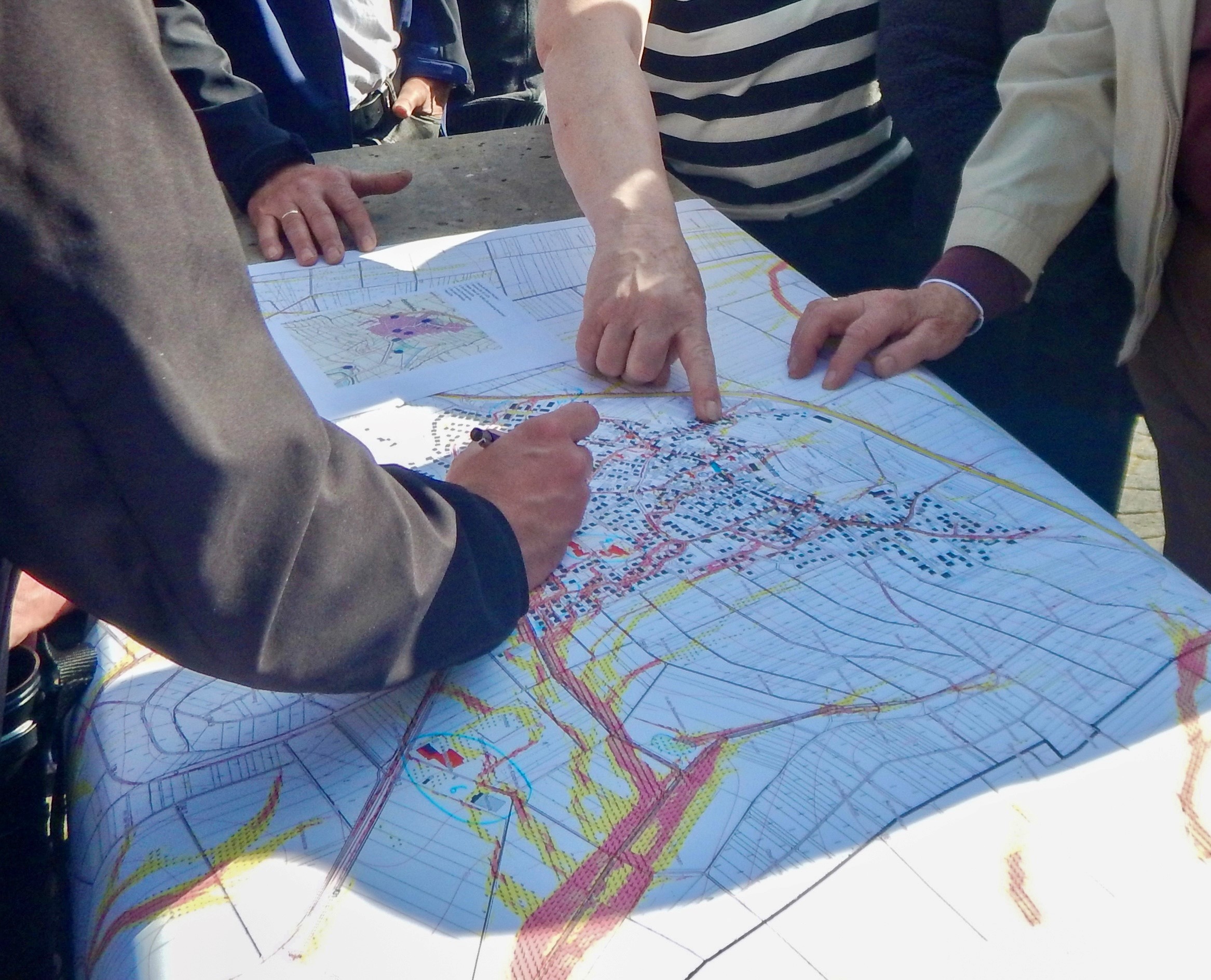 Auf dem Bild erkennt man eine Sturzflutkarte. Diese ist auf einem Untegrund aus Stein ausgelegt. Diverse Menschen zeigen mit ihren Händen auf unterschiedliche Stellen.