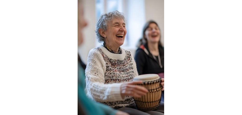 A group of women are gathered in a community center, joyfully participating in a drumming session and laughing together. Music as hobby.