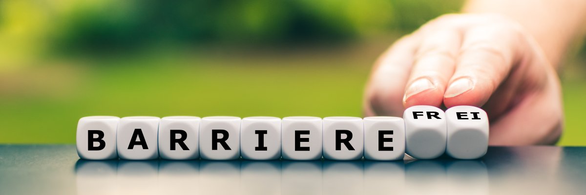 Hand dreht Würfel und ändert das Wort Barriere in barrierefrei Barrierefrei