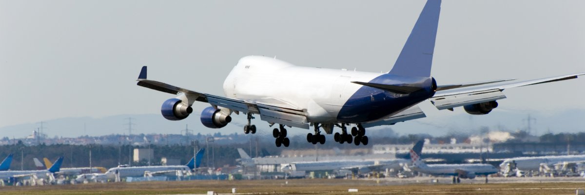 Flugzeug bei Landung Auf dem Bild erkennt man ein weißes großes Flugzeug bei der Landung. Im Hintergrund sind weitere Flugzeuge auf einem Flughafen bzw. Rollfeld zu erkennen.