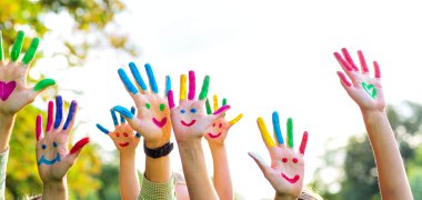 Auf dem Bild erkennt man Kinderhände. Diese sind bunt bemalt und man erkennt mehrere lachende Gesichter.