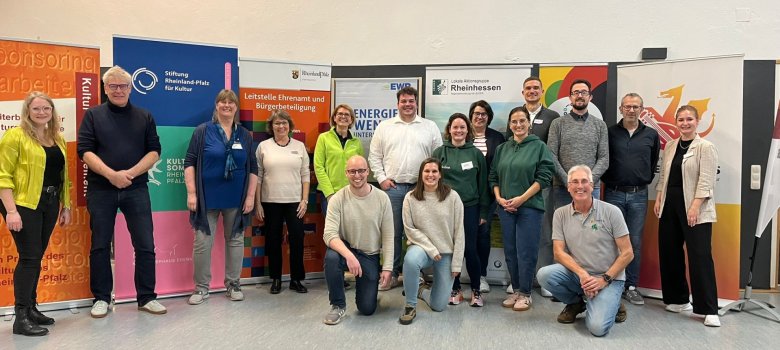 Auf dem Foto erkennt man eine Gruppe von Menschen, welche vor bunten Roll-Ups stehen und in die Richtung des Betrachtenden schauen und dabei freundlich lächeln.