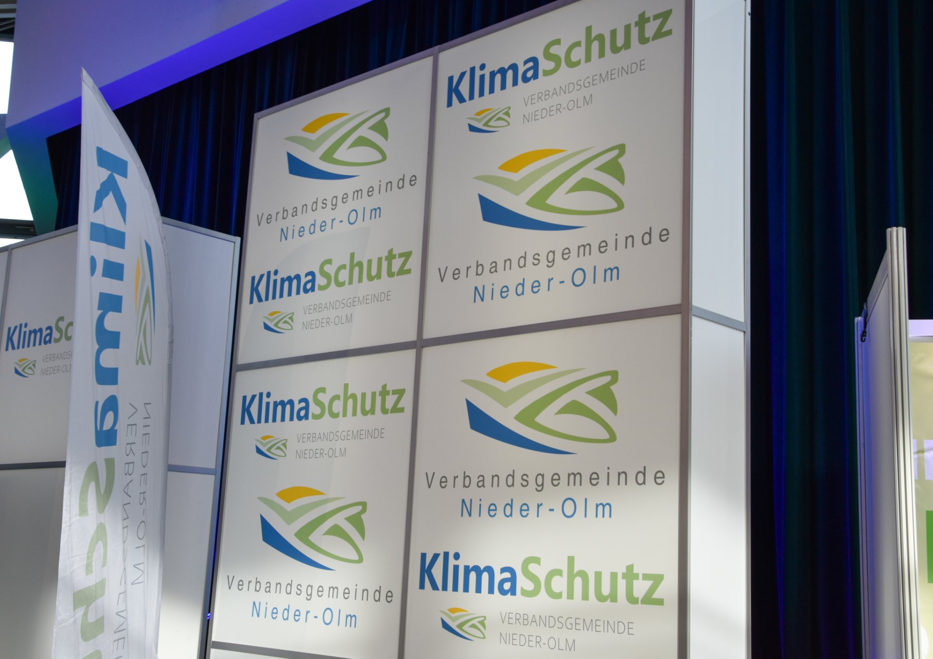 Auf dem Foto erkennt man eine Messewand, auf welchem das Logo des VG-Klimaschutz abgebildet ist.
