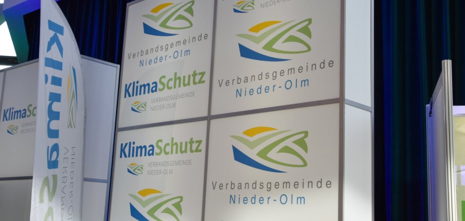 Auf dem Foto erkennt man eine Messewand, auf welchem das Logo des VG-Klimaschutz abgebildet ist.