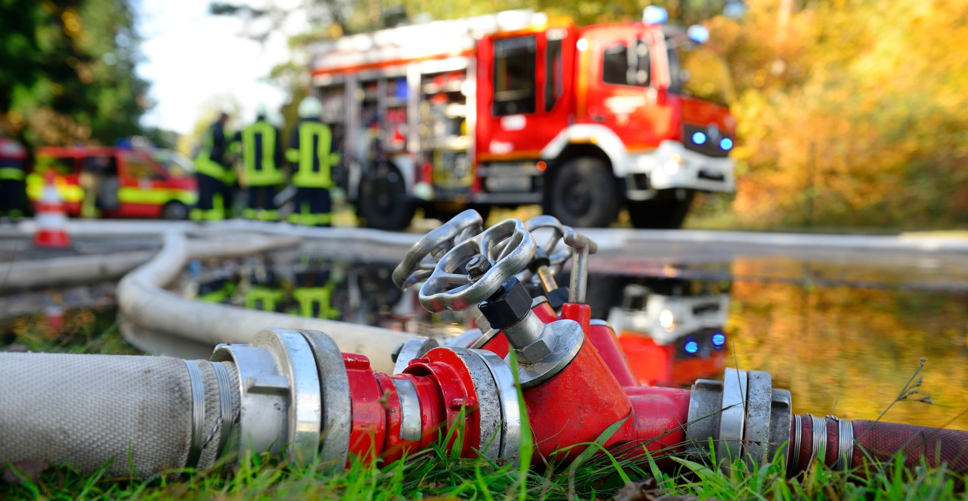 Auf dem Foto sieht man in Entfernung einen Feuerwehrwagen. Im Vordergrund liegen Schläuche.