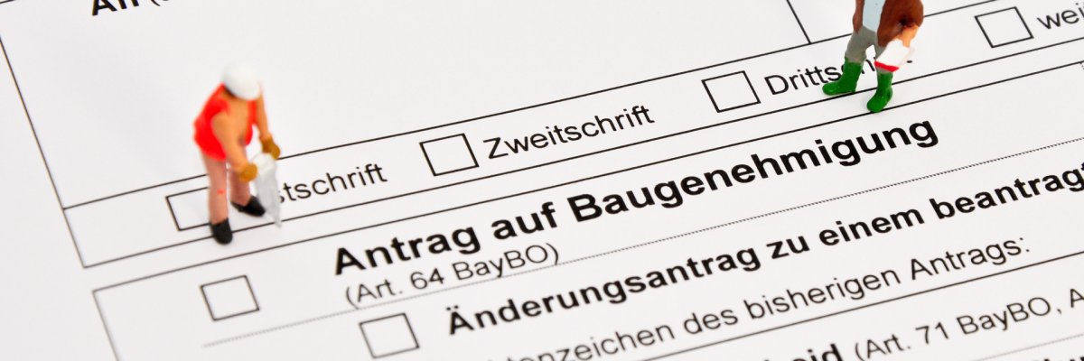 Auf dem Foto erkennt man einen Bauantrag. Links und Rechts sind zwei Männchen zu sehen, welche Bauarbeiter darstellen sollen