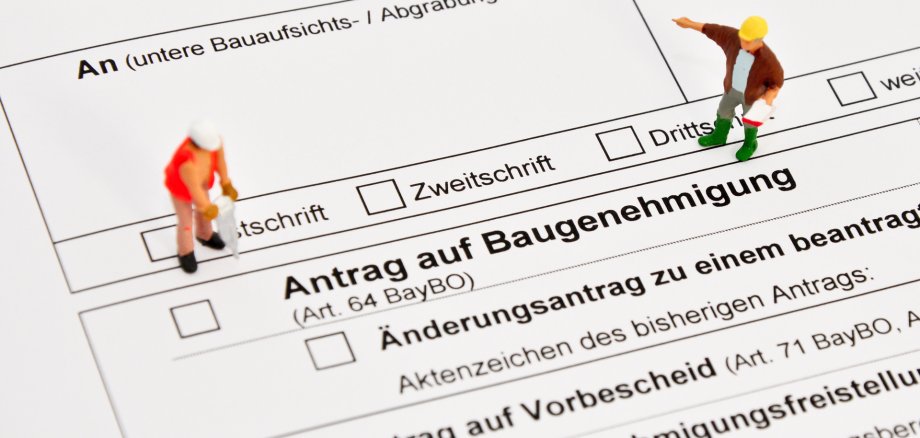 Auf dem Foto erkennt man einen Bauantrag. Links und Rechts sind zwei Männchen zu sehen, welche Bauarbeiter darstellen sollen