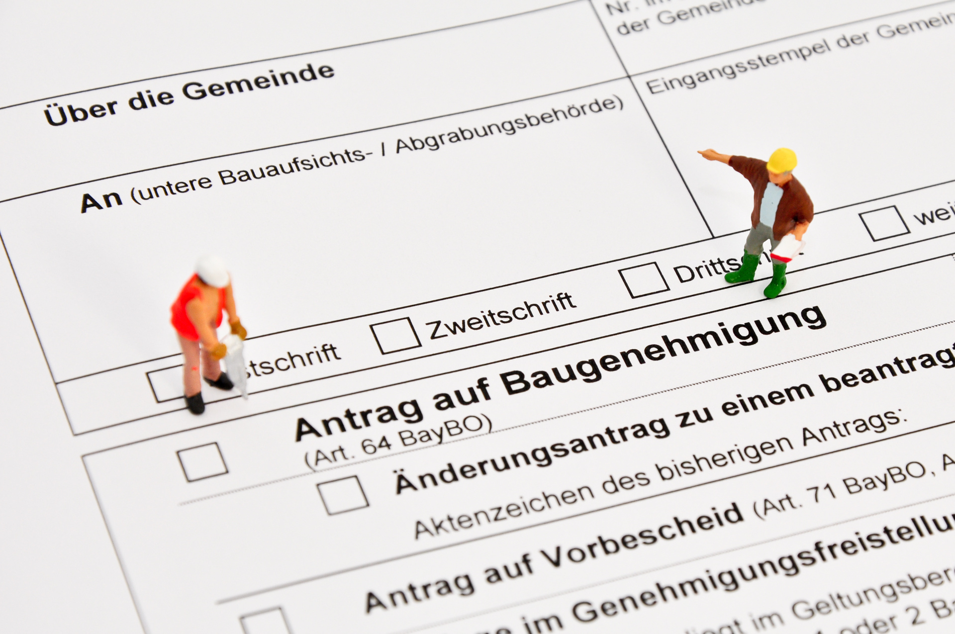 Auf dem Foto erkennt man einen Bauantrag. Links und Rechts sind zwei Männchen zu sehen, welche Bauarbeiter darstellen sollen