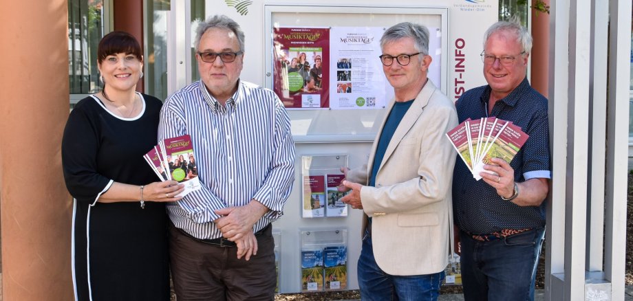 Neue Infostelen am Rathaus Nieder-Olm Auf dem Foto stehen vier erwachsene Personen vor einer Informationsstele. In der Hand halten diese unter anderem Flyer und Prospekte.