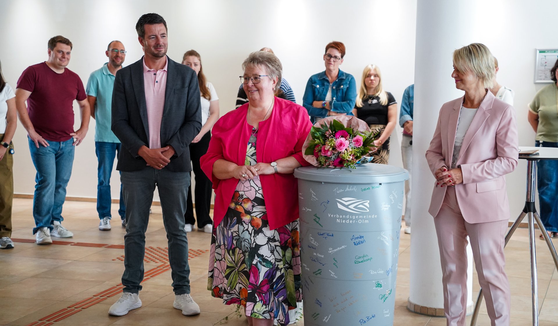 Auf dem Foto erkennt man mehrere Personen, die im Foyer des Rathauses stehen. Zentral sind drei Personen zu erkennen, die rund um eine Regentonne stehen.