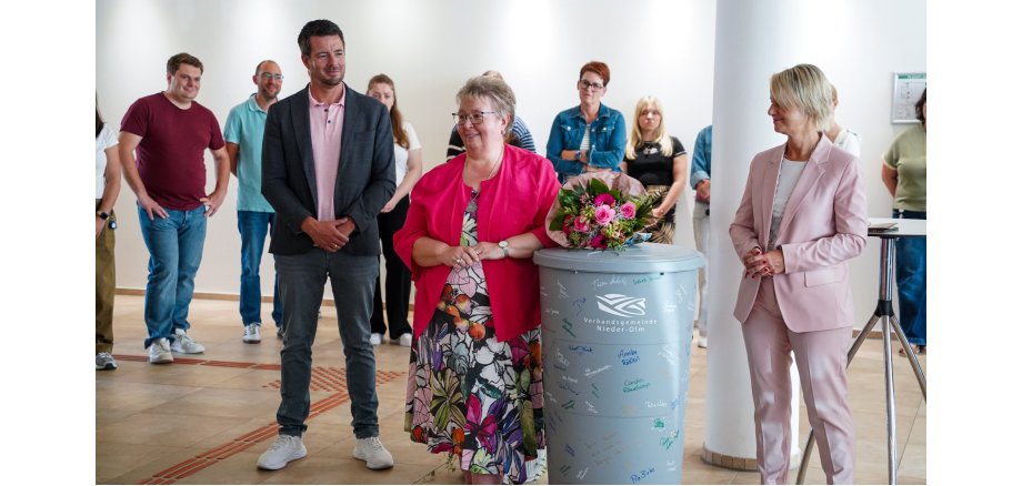 Auf dem Foto erkennt man mehrere Personen, die im Foyer des Rathauses stehen. Zentral sind drei Personen zu erkennen, die rund um eine Regentonne stehen.