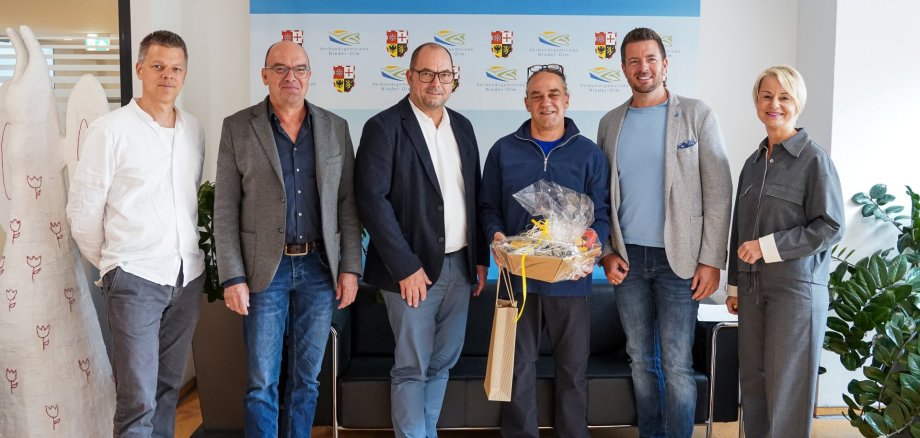 25-jähriges Dienstjubiläum Michael Ernst EIn Gruppenfoto von sechs Personen. Die Person in der Mitte hält ein Präsent in der Hand.