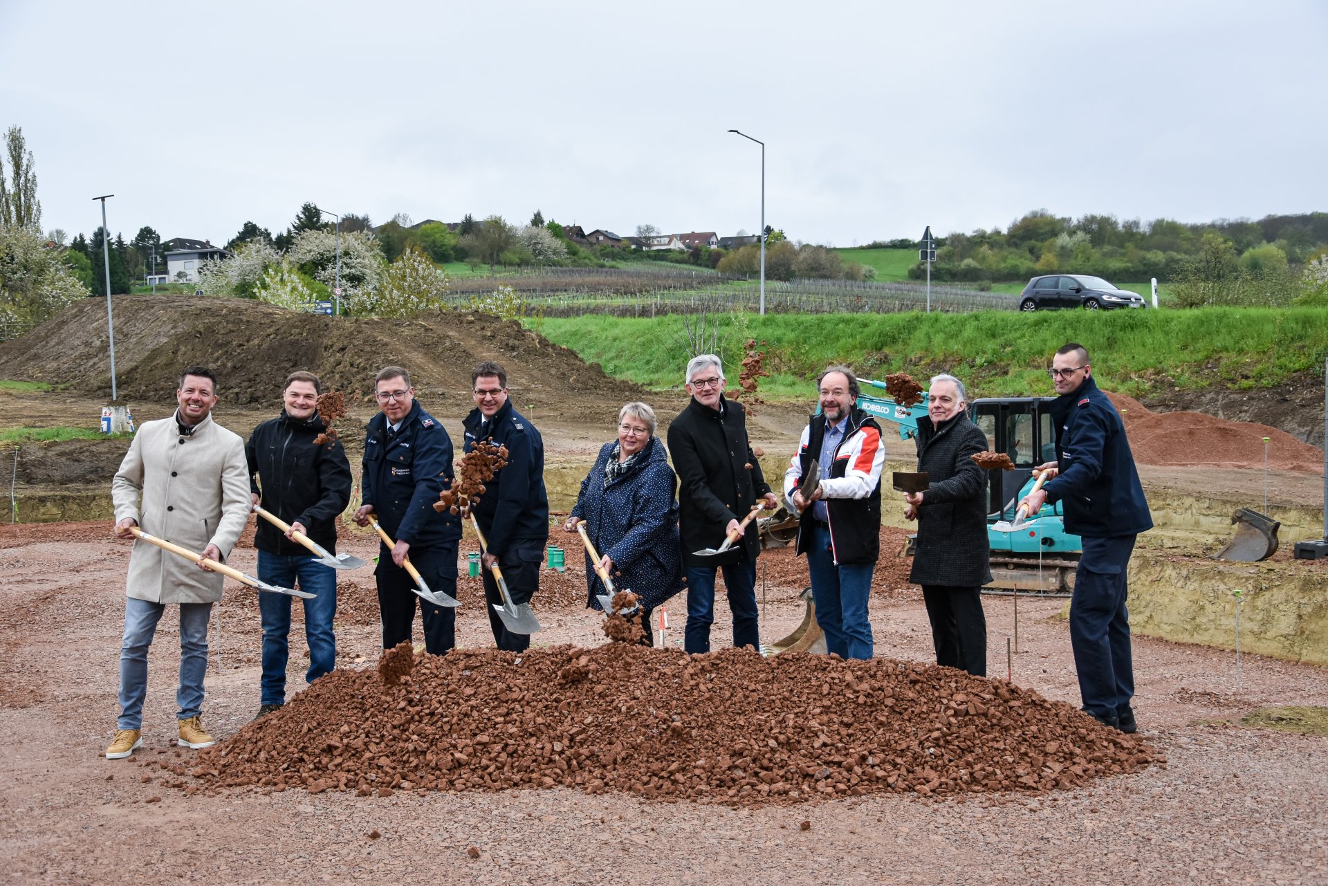 Auf dem Bild erkennt man Menschen mit Schaufeln, die auf einer Baustelle stehen. 