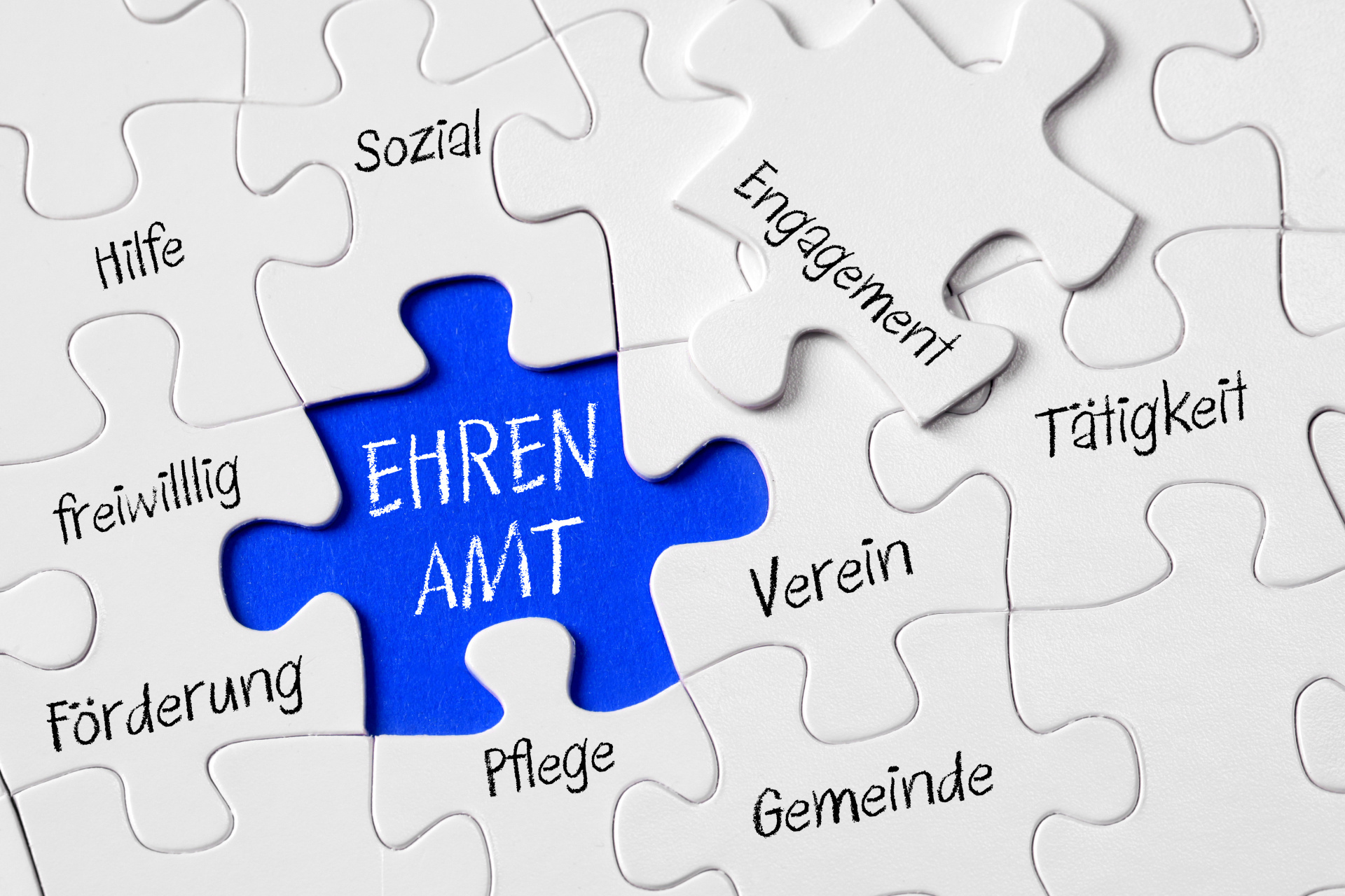 Auf dem Foto erkennt man ein Puzzle. In der Mitte ist ein blaues, freies Feld, in welchem "Ehrenamt" steht. Drum Herum stehen Begriffe wie sozial, Verein, Gemeinde, Tätigkeit.