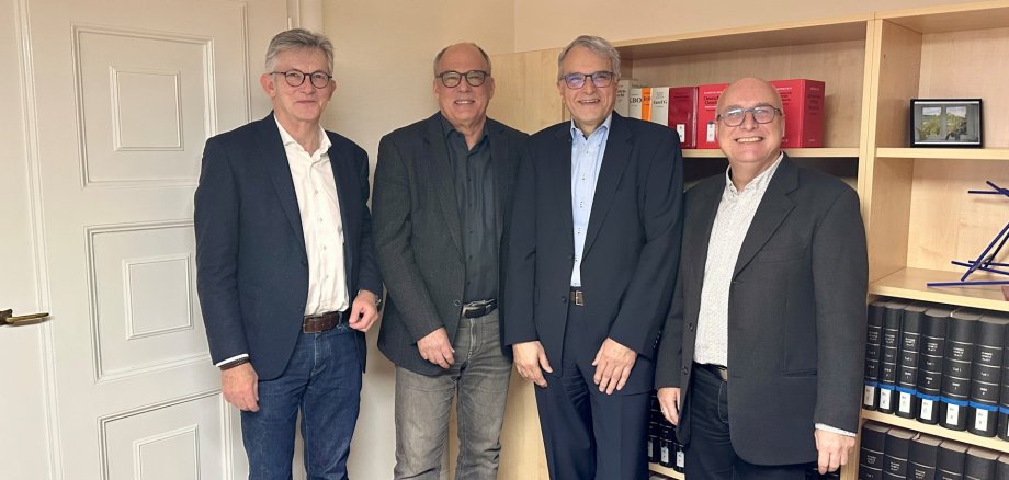 Auf dem Foto erkennt man vier Männer, die vpr einem Bücherregal stehen