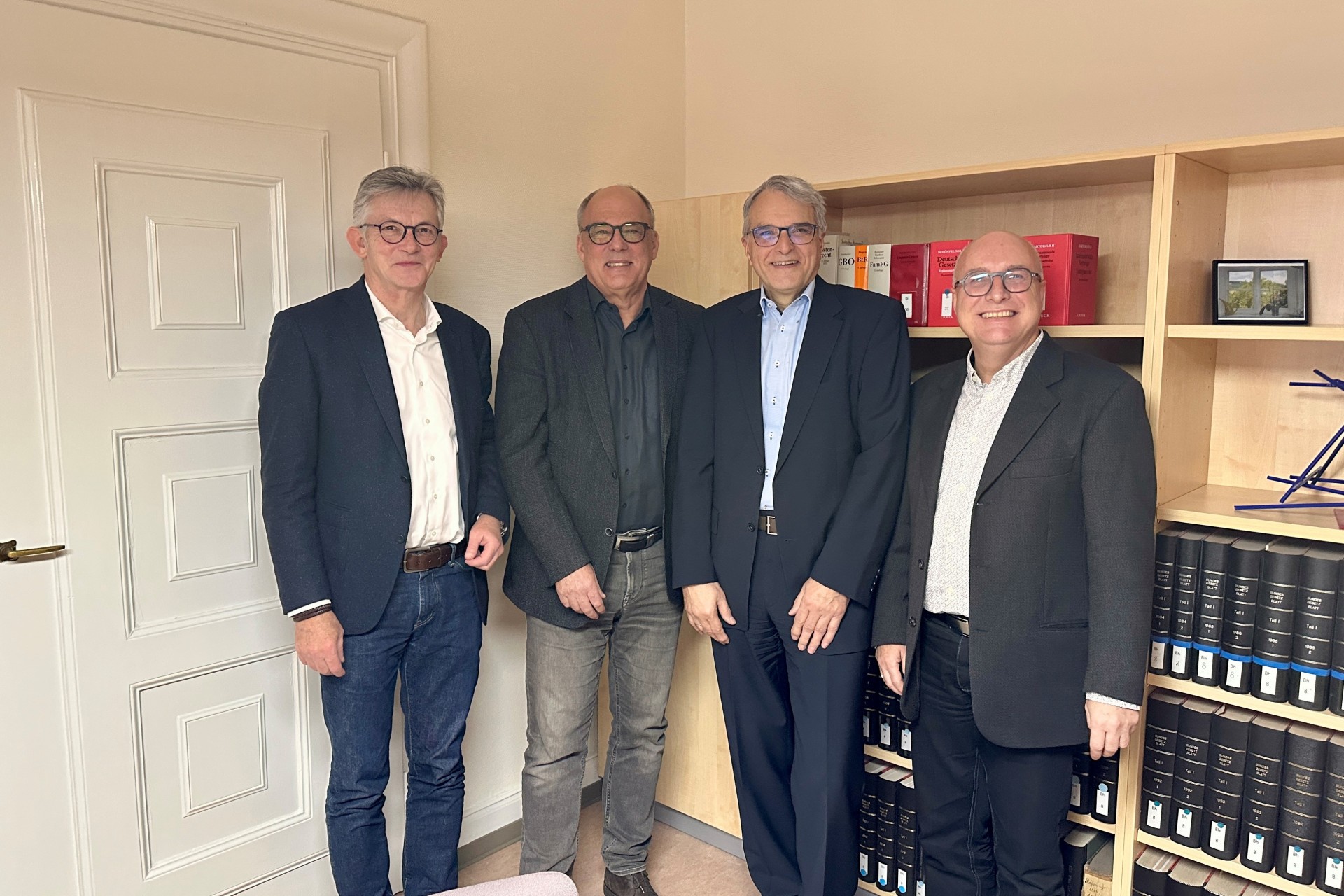 Auf dem Foto erkennt man vier Männer, die vpr einem Bücherregal stehen