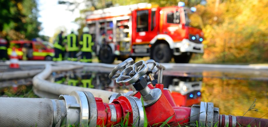 Auf dem Foto sieht man in Entfernung einen Feuerwehrwagen. Im Vordergrund liegen Schläuche.